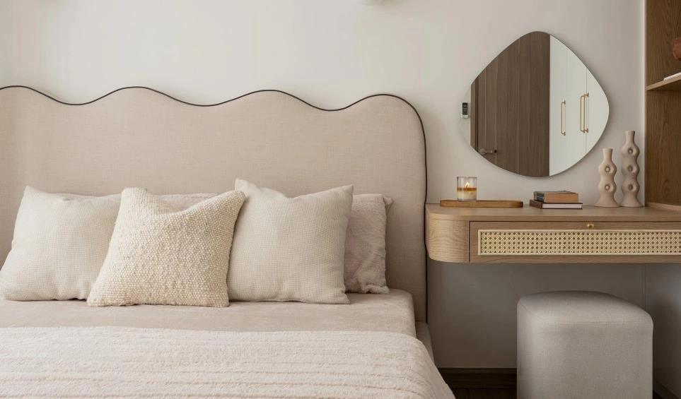 Floating light-wood dressing table placed beside the bed in a small apartment bedroom.