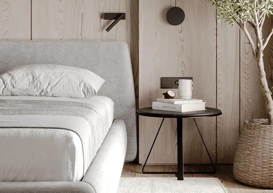 Minimal black round table used as a bedside table in a small apartment bedroom.