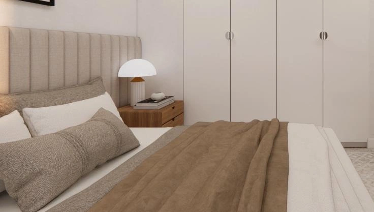 Small bedroom with a light brown fabric couple bed and layered neutral pillows creating a warm, stylish couple&rsquo;s space.