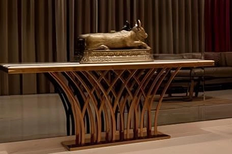 Gold metal bull figurine displayed on a modern metal stand in a small apartment living room.